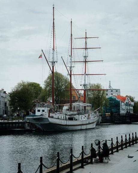 Ein großes Schiff mit roten Masten liegt unter einem bewölkten Himmel an einem Uferweg vor Anker.