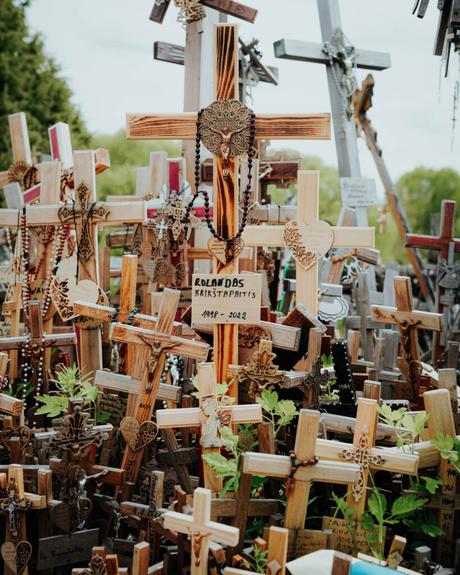 Viele Holzkreuze mit Rosenkränzen und Gedenktafeln drängen sich auf einer Gedenkstätte im Freien.