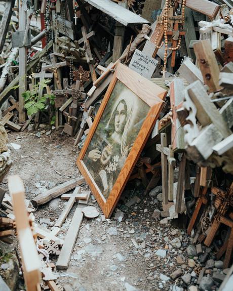 Ein gerahmtes religiöses Porträt lehnt zwischen vielen Holzkreuzen und Rosenkränzen auf einem Kiesweg.