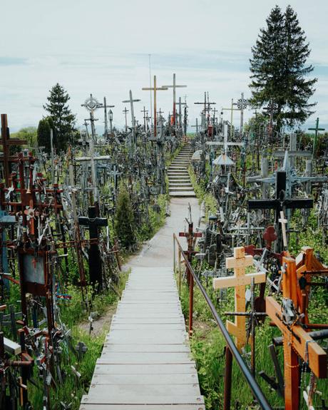 Holzsteg, der über einen Hügel führt, der mit vielen Kreuzen unterschiedlicher Größe und Art bedeckt ist.