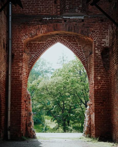 Gotischer Backsteintorbogen, der grüne Bäume und Sonnenlicht draußen einrahmt.