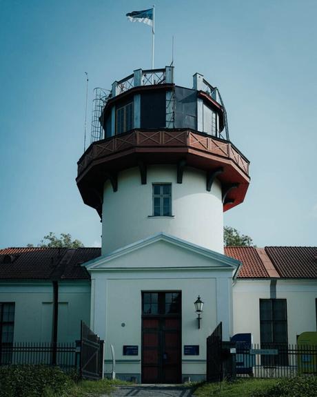 Ein hohes, rundes weißes Gebäude mit einem roten Dach und einer Flagge darauf, vor einem klaren blauen Himmel.