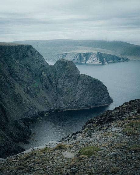Steile Felsklippen und ein ruhiges Meer unter einem wolkenverhangenen Himmel in einer abgelegenen Küstenlandschaft.