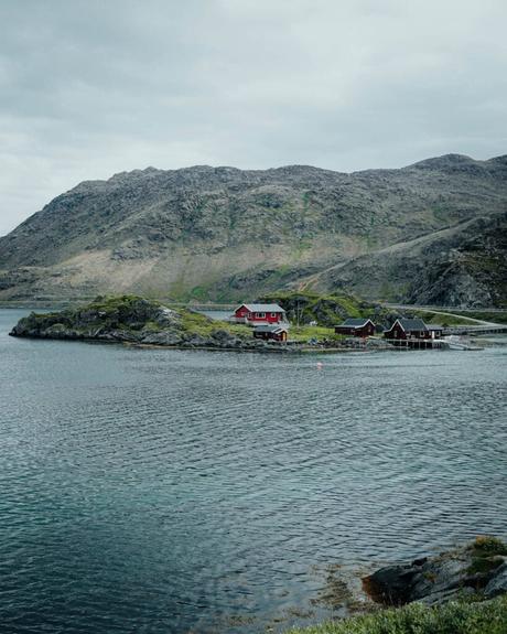 Die roten Hütten liegen auf einer kleinen, felsigen Insel, die von Wasser umgeben ist, mit Bergen im Hintergrund.