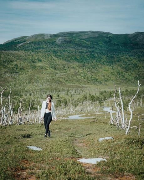 Eine Frau geht auf einem von Bäumen umgebenen Grasweg, mit einem grünen Berg im Hintergrund.
