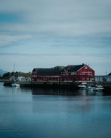 Rote Gebäude und angedockte Boote am ruhigen Wasser unter einem bewölkten Himmel in einem Küstendorf.
