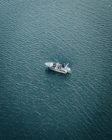Ein kleines Motorboot mit fischenden Menschen schwimmt auf dem ruhigen, gekräuselten blauen Wasser.