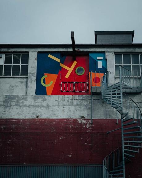 Eine Wendeltreppe führt zu einem Gebäude, auf dessen obere Wand bunte geometrische Formen gemalt sind.