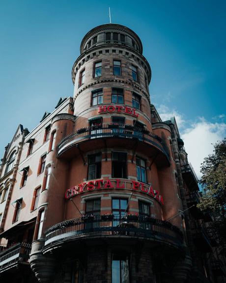 Historisches Backsteingebäude mit rundem Turm, rotem Neonschild Hotel Crystal Plaza und Balkonen unter blauem Himmel.