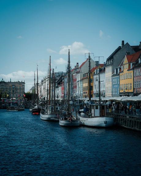 Segelboote, die an einem Kanal mit bunten Gebäuden in einer europäischen Stadt unter blauem Himmel angedockt sind.