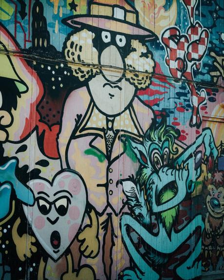 Buntes Graffiti, das einen Cartoon-Mann im Anzug, eine Herzfigur und ein grünes Wesen mit übertriebenen Gesichtszügen zeigt.