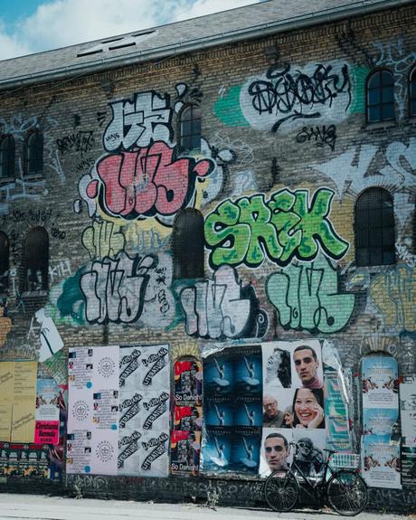 Ein Backsteingebäude mit bunten Graffiti und Plakaten, davor ein abgestelltes Fahrrad.