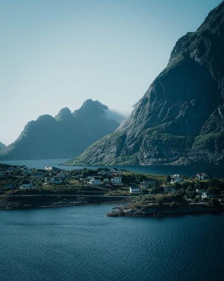 Kleines Küstendorf am tiefblauen Wasser, umgeben von steilen, felsigen Bergen unter einem klaren Himmel.