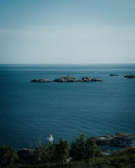 Ein kleiner Leuchtturm auf einer felsigen Insel, umgeben von ruhigem, blauem Meer und klarem Himmel.