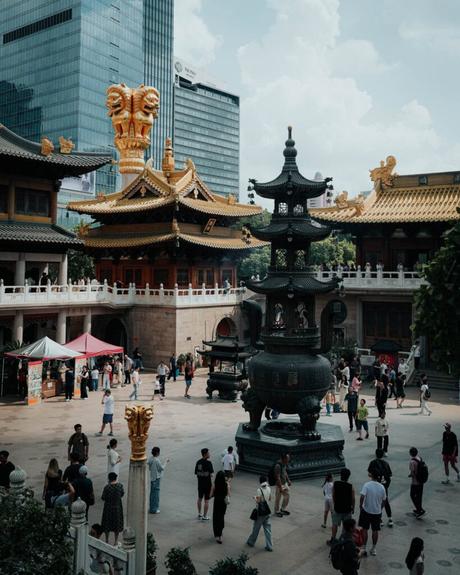 Menschen spazieren in einem Innenhof eines traditionellen Tempels mit goldenen Dächern, umgeben von modernen Hochhäusern.