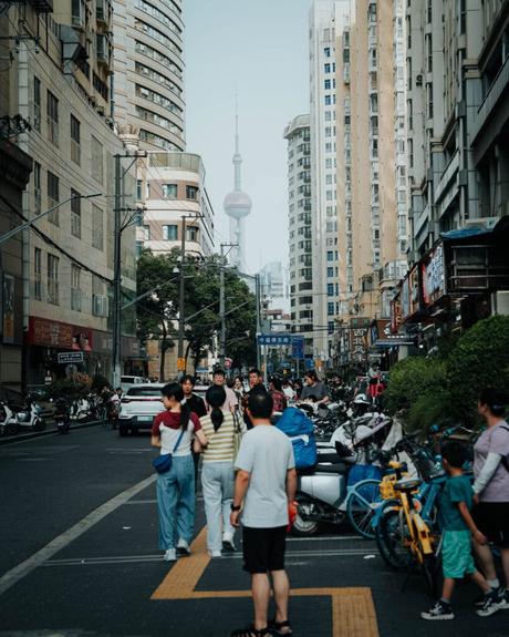 Menschen gehen entlang einer belebten Straße mit hohen Gebäuden und einem Turm im Hintergrund.