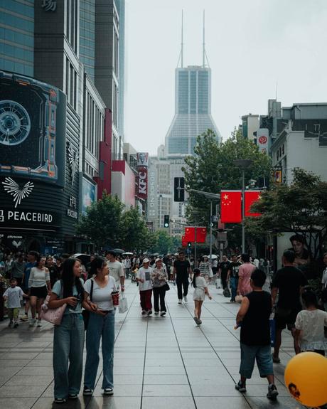 Belebte Stadtstraße in China mit Menschen, die spazieren gehen, chinesischen Flaggen, Geschäften und hohen Gebäuden im Hintergrund.