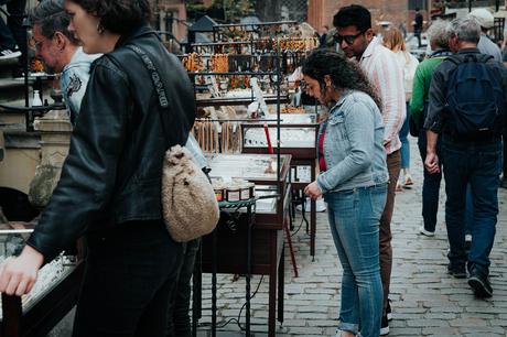 Menschen, die an Marktständen in einer Kopfsteinpflasterstraße im Freien nach Schmuck stöbern.