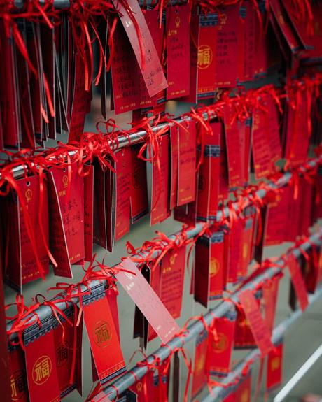 Rote Gebetszettel mit chinesischer Schrift hängen an roten Schnüren in Reihen, wahrscheinlich in einem Tempel oder Schrein.