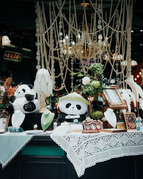 Plüschpandas, Schmuck und Blumen auf einem mit Spitze bedeckten Tisch mit Perlenverzierungen darüber.