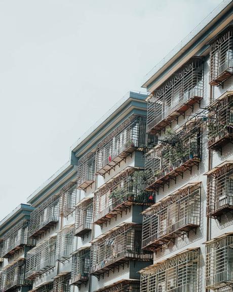 Mehrfamilienhaus mit vielen Balkonen, die mit Metallgittern und einigen Pflanzen bedeckt sind, von einem niedrigen Winkel aus gesehen.