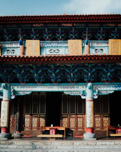 Farbenfrohe traditionelle chinesische Tempelfassade mit verschnörkelten Mustern, Säulen und goldenen Inschriften über dem Eingang.