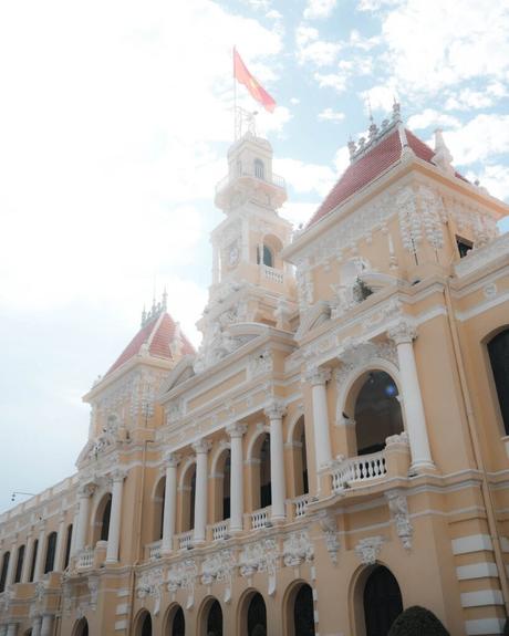Cremefarbenes Gebäude im französischen Kolonialstil mit rotem Dach, verzierten Details und einer Fahne auf dem Dach, unter einem strahlenden Himmel.