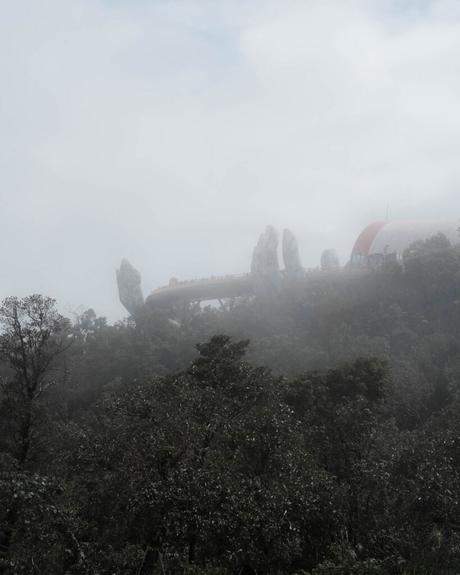 Eine neblige Brücke mit riesigen Steinhänden erhebt sich an einem nebligen Tag über dichte grüne Bäume.