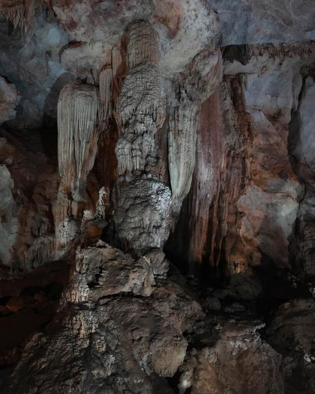 Große Stalaktiten und Stalagmiten in einer schwach beleuchteten Höhle mit strukturierten Felsformationen.