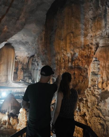Zwei Personen auf einem Steg im Inneren einer großen, beleuchteten Höhle mit beeindruckenden Felsformationen.