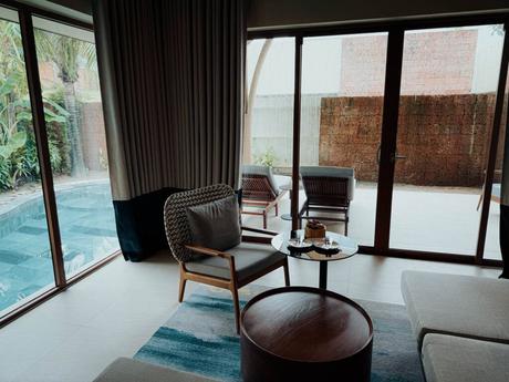 Modernes Wohnzimmer mit Glastüren, die zur Terrasse und zum Pool führen, mit gemütlichen Sesseln und einem Couchtisch.