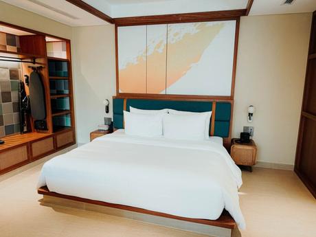 Modernes Hotelzimmer mit einem großen, sauber gemachten Bett, Holzmöbeln und einem offenen Schrank.