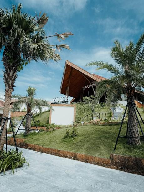 Modernes Gebäude mit schrägem Dach, Palmen und YOGO-Schild unter blauem Himmel.