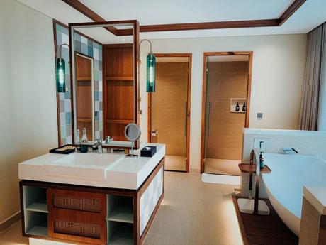 Modernes Badezimmer mit Flügeltüren, einer Badewanne, einem Waschbecken mit Spiegel und grünen Pendelleuchten.