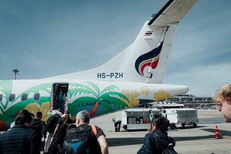 Reisende besteigen ein buntes Flugzeug mit Palmenkunst auf einem Flughafen unter einem klaren blauen Himmel.