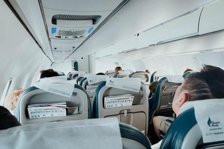 Blick aus dem hinteren Teil einer Flugzeugkabine mit sitzenden Passagieren und geschlossenen Gepäckfächern.