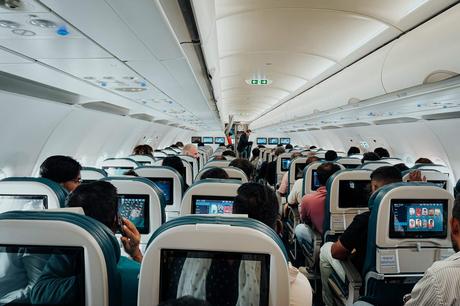 Passagiere, die in einer Flugzeugkabine sitzen, auf Bildschirme schauen und sich auf den Start vorbereiten.