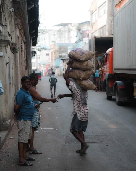 Ein Mann, der schwere Säcke auf dem Kopf trägt, schüttelt einem anderen Mann auf einer belebten Straße die Hand.