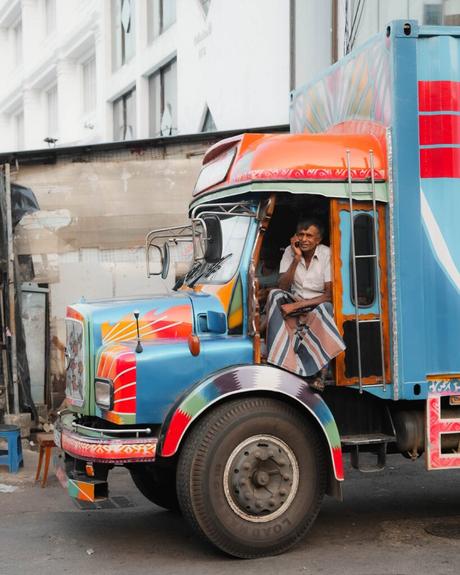 Ein Mann in einem farbenfrohen Lastwagen telefoniert mit einem Handy, während er in der Tür einer Stadtstraße sitzt.