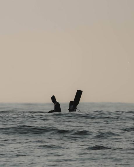 Silhouette einer Person im Meer neben einem kleinen Bootsmotor in der Abend- oder Morgendämmerung.