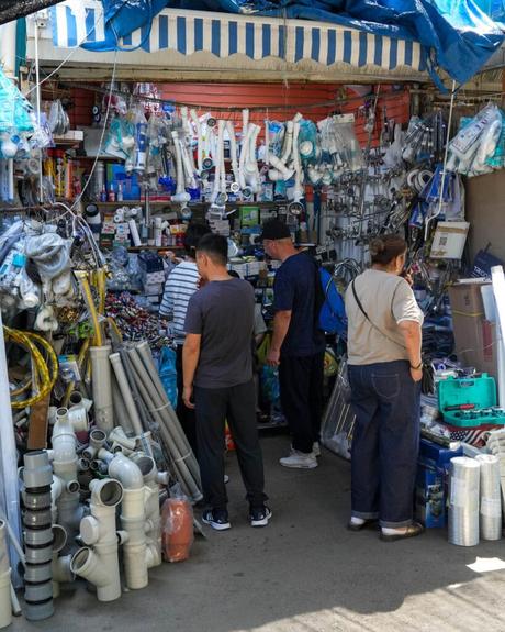 An einem gut besuchten Marktstand im Freien, an dem Rohre und Armaturen ausgestellt sind, sehen sich die Leute Sanitärbedarf an.