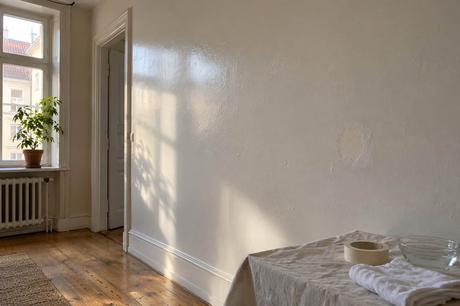 Glänzend gestrichene helle Wand im seitlichen Fensterlicht, davor Abdecktuch, Klebeband und Wasserschale.