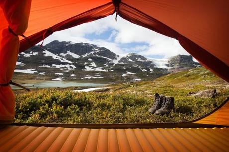 Der Blick aus einem Zelt mit einer Isolationsmatte darin und davor ein paar Wanderschuhe mit einem herrlichen Blick auf eine Berglandschaft