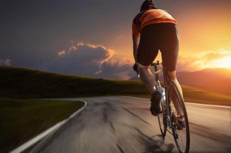 Ein Rennradfahrer fährt auf einer Straße dem Sonnenuntergang entgegen.