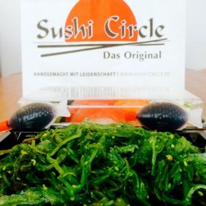 Grüner Wakamesalat mit zwei Sojasoßen-Fischen und der Tüte von Sushi Circle Hamburg