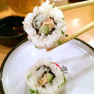 Zwei Sushi-Rollen mit Lachs und Gurke, eins von zwei Stäbchen gehalten