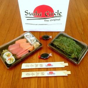 Eine Sushi Box, ein Wakamesalat, zwei Sojasoßen-Fische, zwei Paar Essstäbchen und die Tüte vom Sushi Circle Hamburg