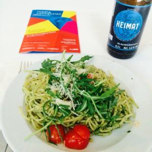 Pesto Spaghetti mit Rucola, Cherrytomaten und Parmesan, daneben das Heimat Bier und ein Programmheft
