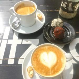 ein Cappuccino mit Herzmuster im Milchschaum, ein Café Crème und zwei Energiebälle